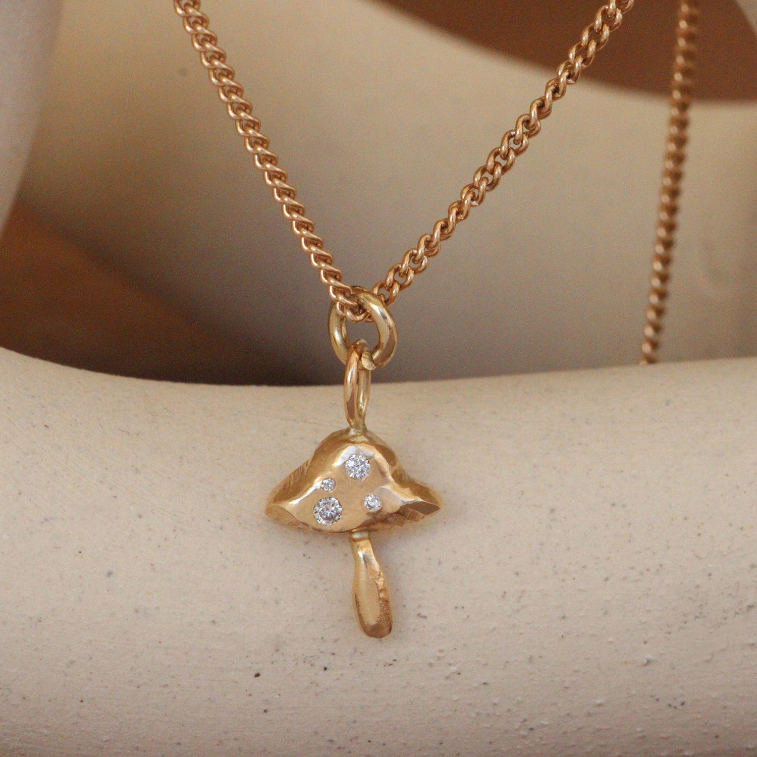 Lifestyle close up view of Mushroom Charm / Round Natural Diamonds by Oxbow Designs hanging over a ceramic with a blurred background
