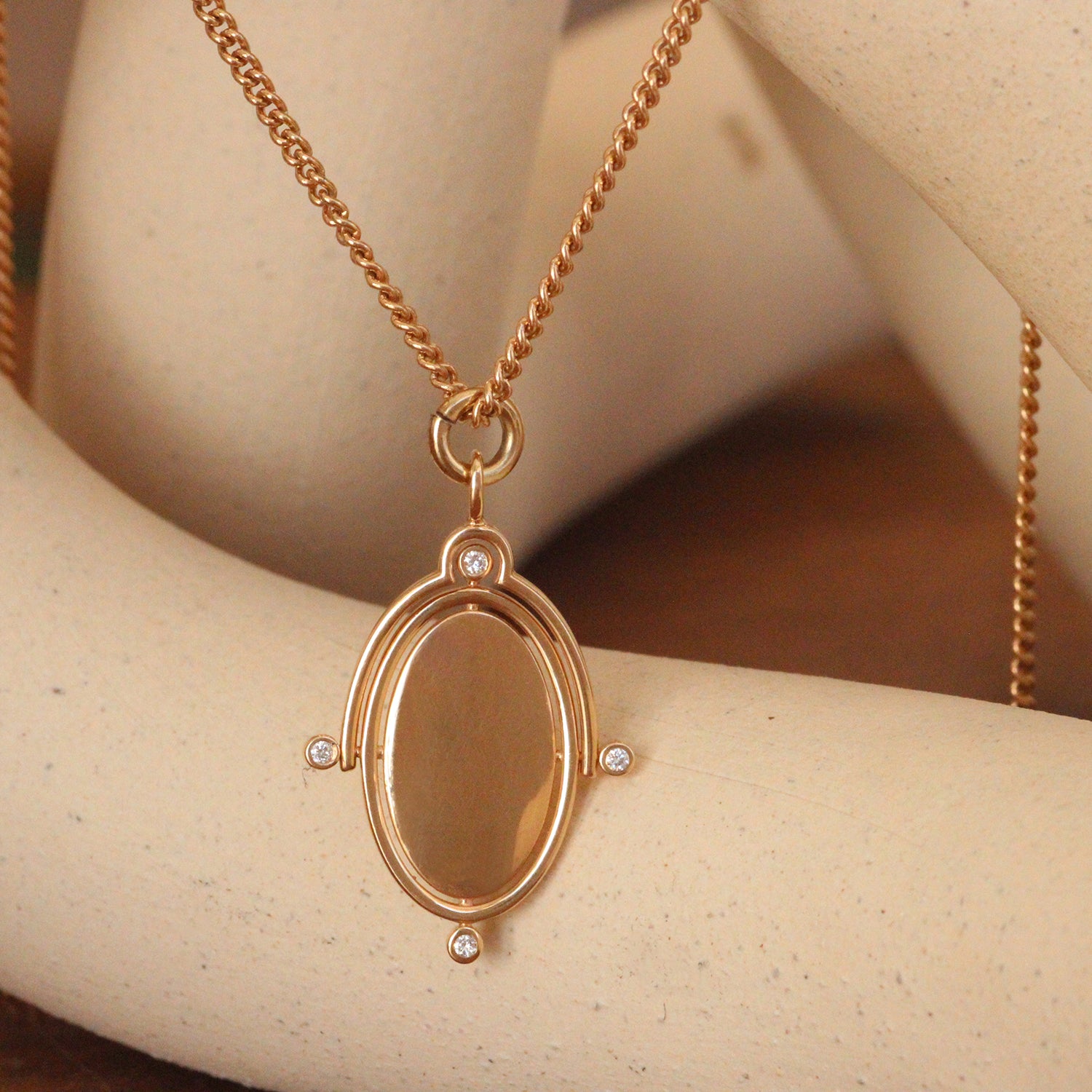 Lifestyle close up view of Perpetuum Charm / Flush Round Natural Diamonds by Sandy Rubin hanging over a ceramic with a blurred background