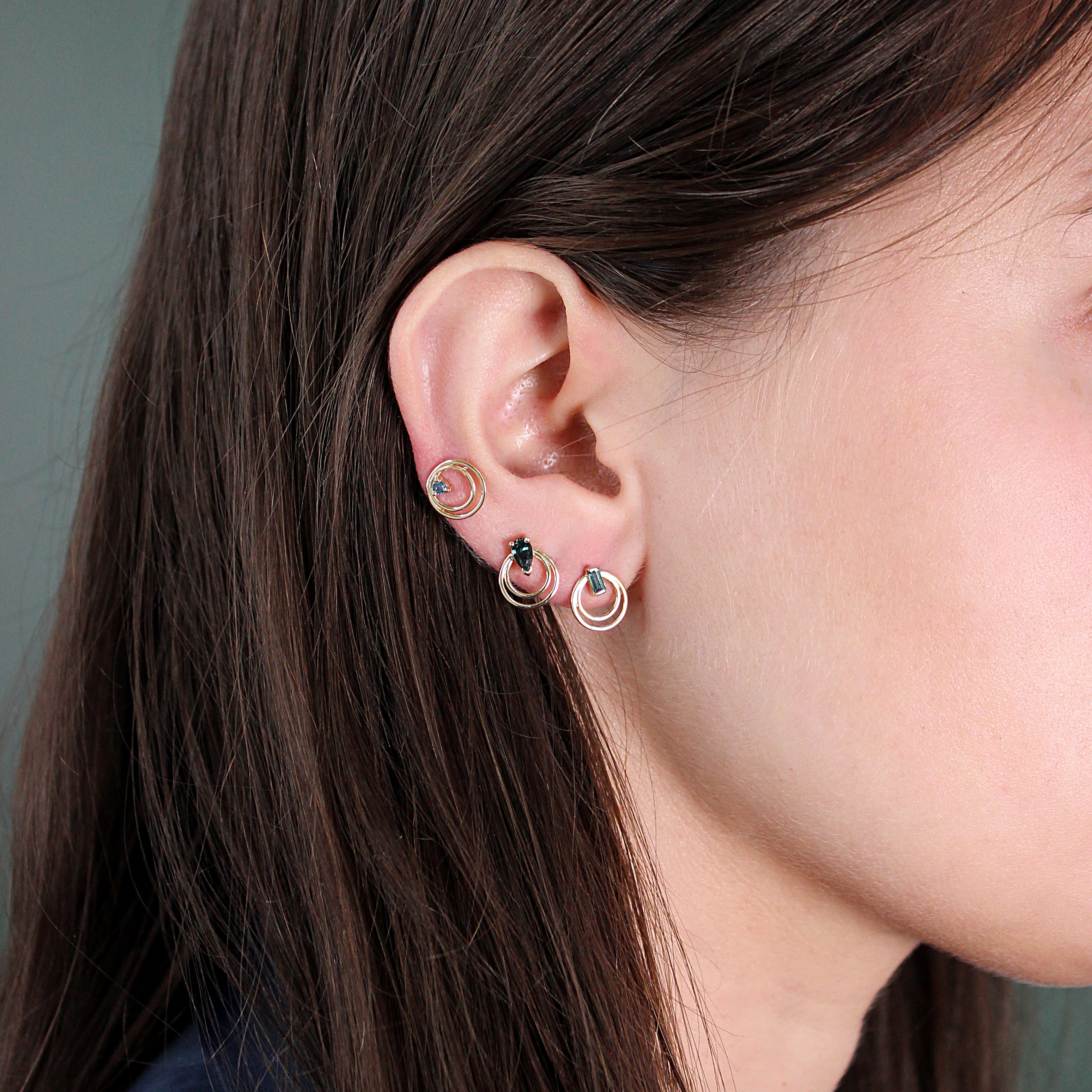 Model wears Ripple Earring / Round Sapphire, Ripple Earring / Pear Sapphire, and Ripple Earring / Lab Green Baguette Diamond by Goldpoint Jewelry in ear