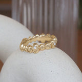 Lifestyle angled view of Ruins Band Medium Flush Round Lab Diamonds in 14k Yellow Gold by Goldpoint Jewelry on a ceramic with a blurred background