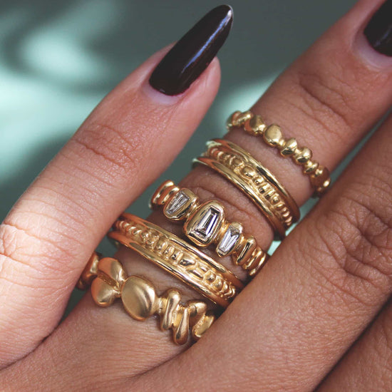 Model wears stack of Ruins collection bands on ring finger including Ruins Band / Polished Sides