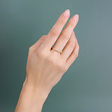 Model wears Ruins Band / Thin in 14k yellow gold by Goldpoint Jewelry on middle finger with a teal backdrop