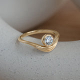 Lifestyle angled side view of Event Horizon Ring / Round Natural Diamond 0.50ct by Sandy Rubin on a ceramic with a blurred neutral background