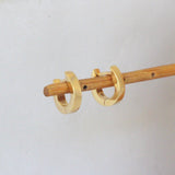 Lifestyle angled side view of Solid Huggie Hoops by Mon Pilar on a wooden stand with blurred backgroud