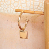 Lifestyle angled view of Step Frame Charm / Square on a Cornice Hoop by Goldpoint Jewelry on a wooden earring display