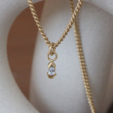 Lifestyle front view of Step Split Bezel Charm / Lab Pear Diamond on a chain by Goldpoint Jewelry hanging over a ceramic with a blurred background