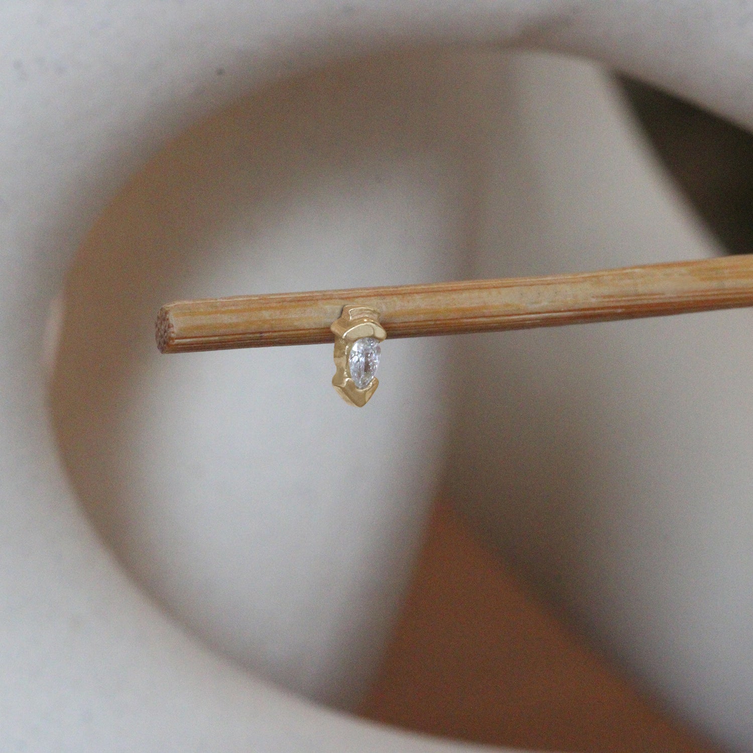 Lifestyle angled view of  Step Earring / Lab Pear Diamond by Goldpoint Jewelry on a wooden stand with a blurred background