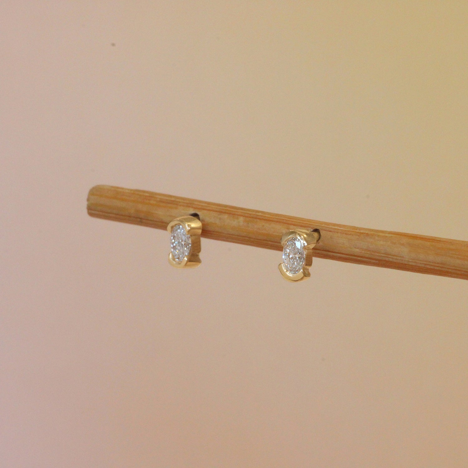 Lifestyle angled view of Split Bezel Earring / Lab Oval Diamond by Goldpoint Jewelry on a wooden stand with a gradient background