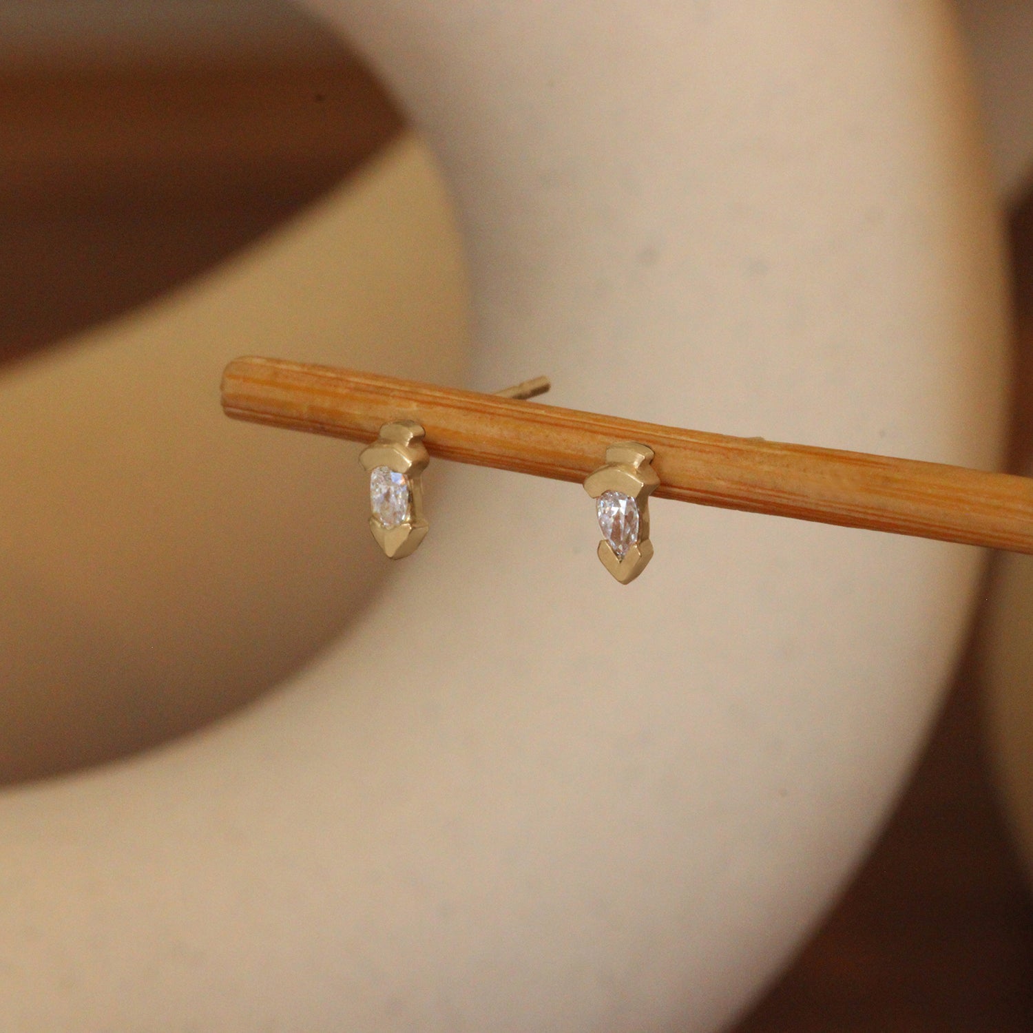 Lifestyle angled view of a pair of Step Earring / Lab Pear Diamond pieces by Goldpoint Jewelry on a wooden stand with a blurred background