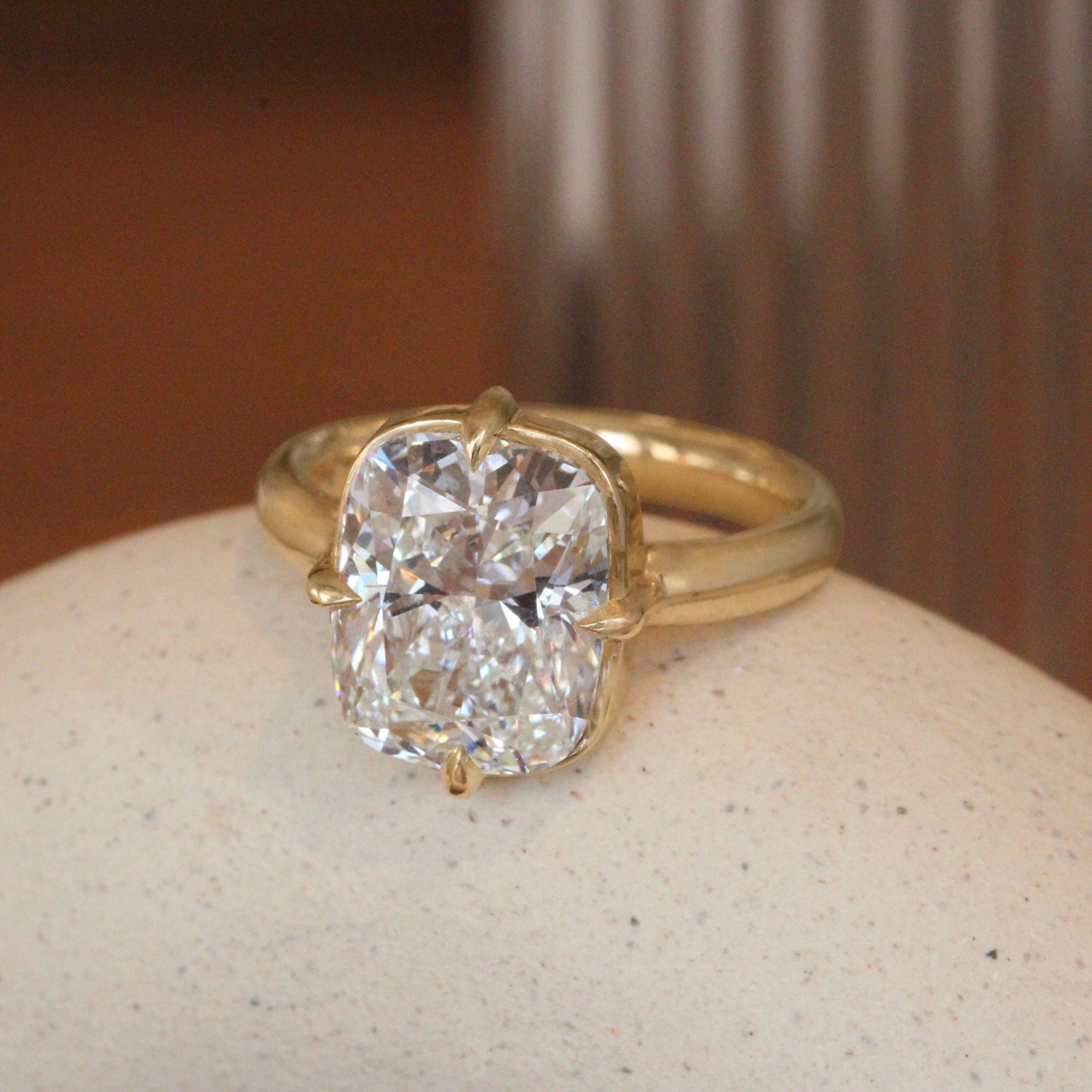 Lifestyle angled view of Sutton Ring Cushion Lab Diamond 5.08ct by Goldpoint Jewelry on a ceramic with blurred background