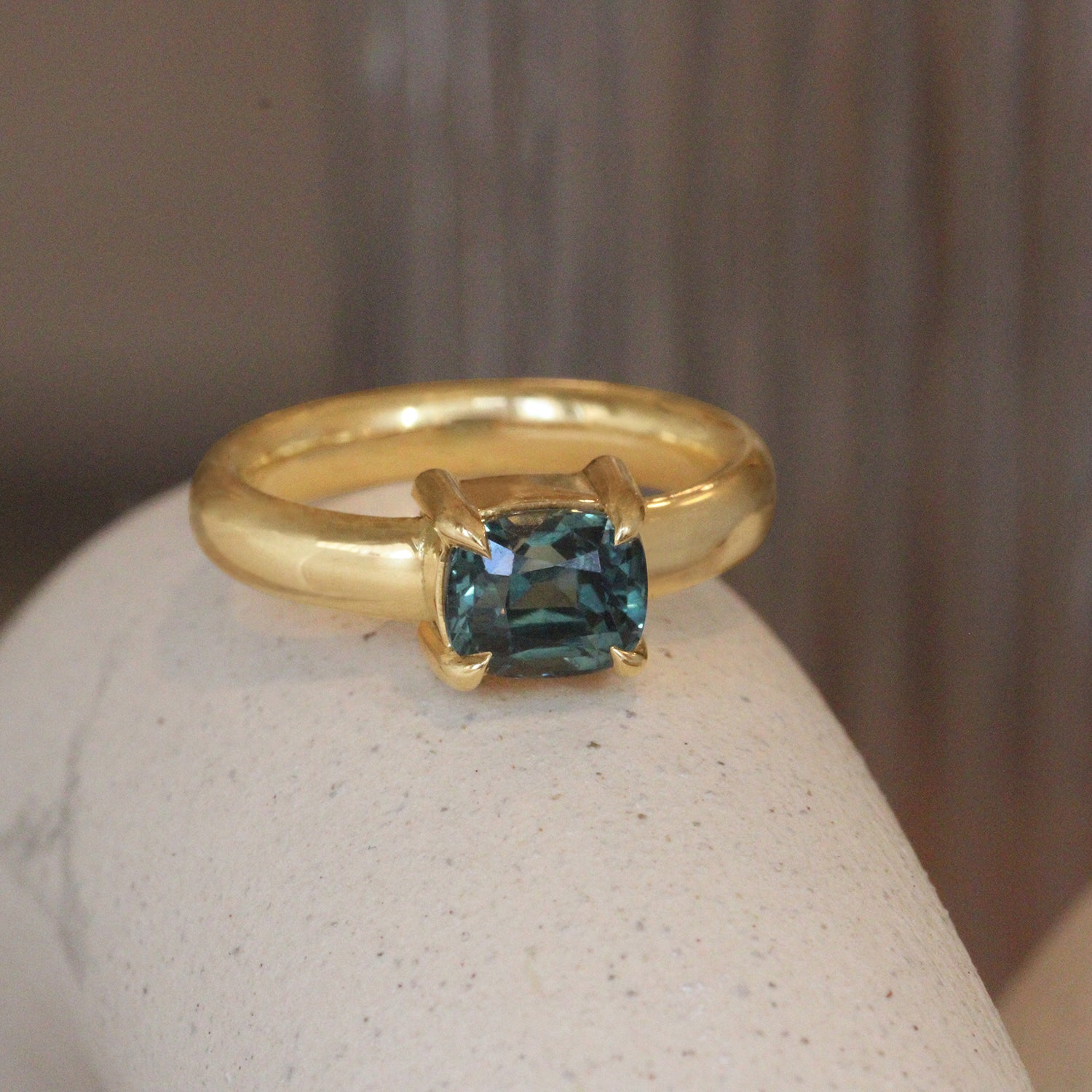 Lifestyle angled view of Sutton Ring Cushion Cut Sapphire 2.03ct by Goldpoint Jewelry on a ceramic with blurred background