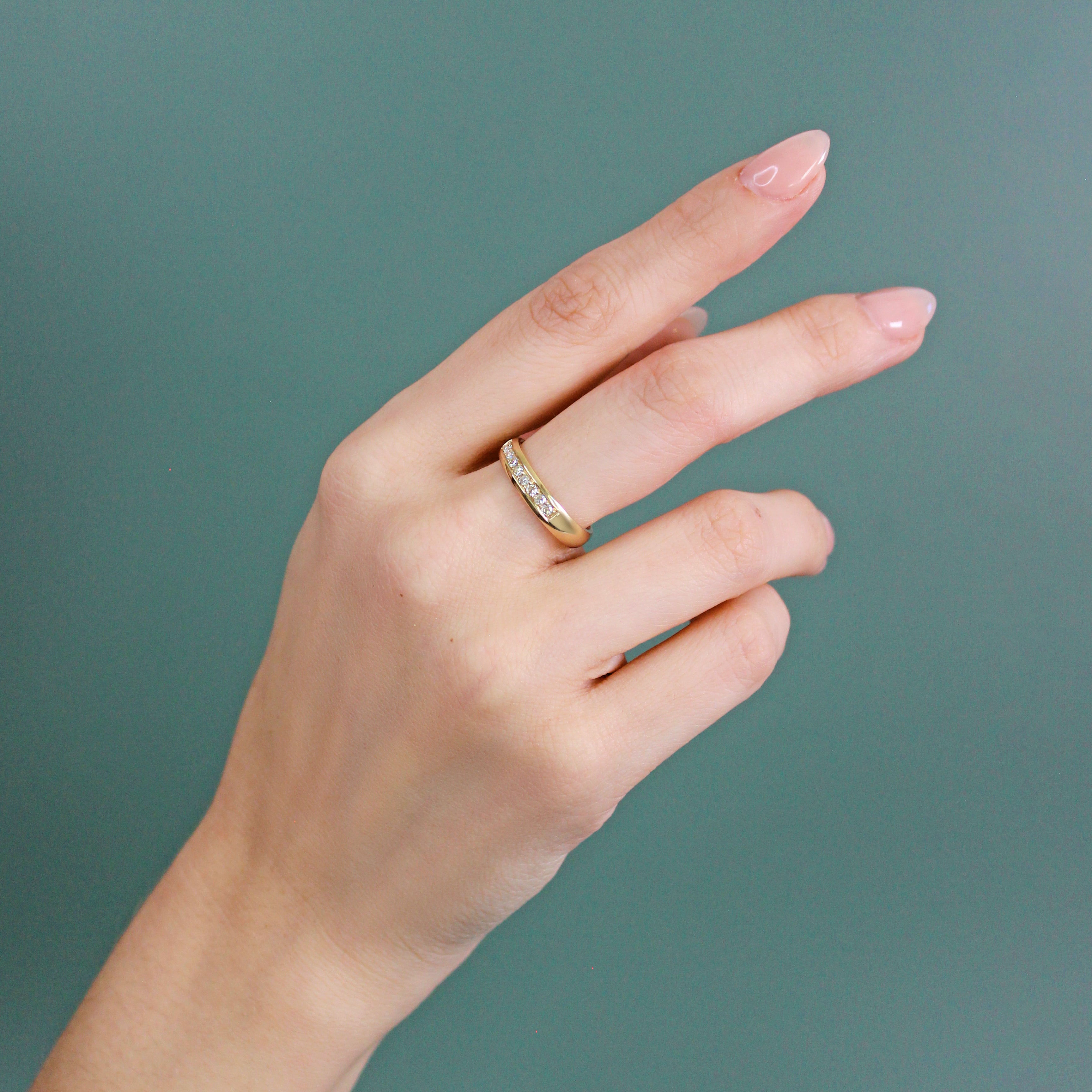 Model wears Dome Band Thick 4mm / Bright Cut Rose Cut Diamonds in 14k yellow gold by Goldpoint Jewelry on middle finger on teal background