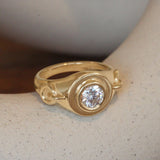 Lifestyle angled view of Vessel Pinky Ring in 14k yellow gold by Amour Vee on a ceramic on a blurred background