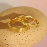 Lifestyle stacked view of Waves Wide Band in 18k yellow gold and Waves Band in 14k yellow gold