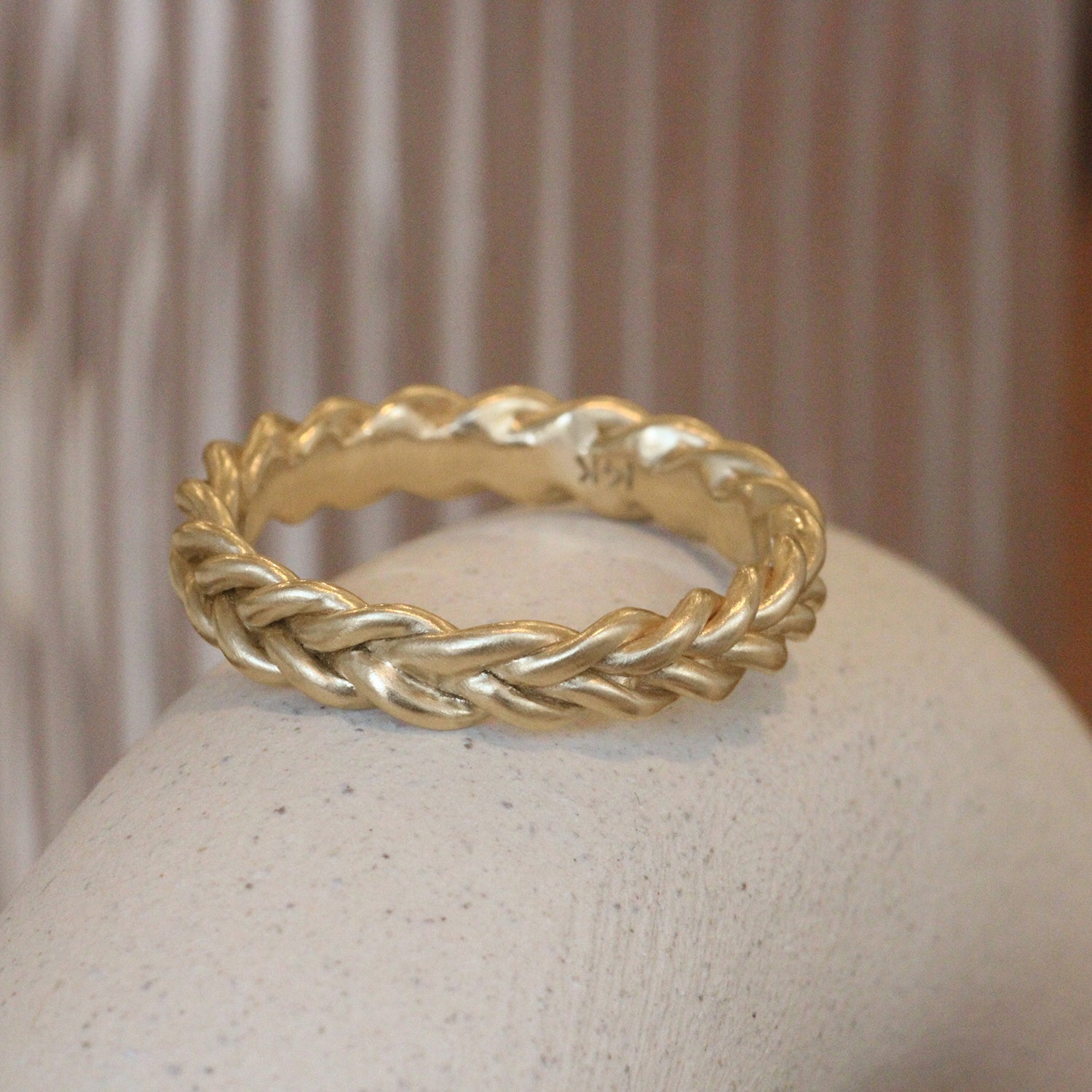 Lifestyle angled view of Wide Kismet Band in 14k yellow gold by Leili Kasraie Studio on a ceramic with a blurred background