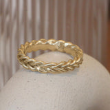 Lifestyle angled view of Wide Kismet Band in 14k yellow gold by Leili Kasraie Studio on a ceramic with a blurred background