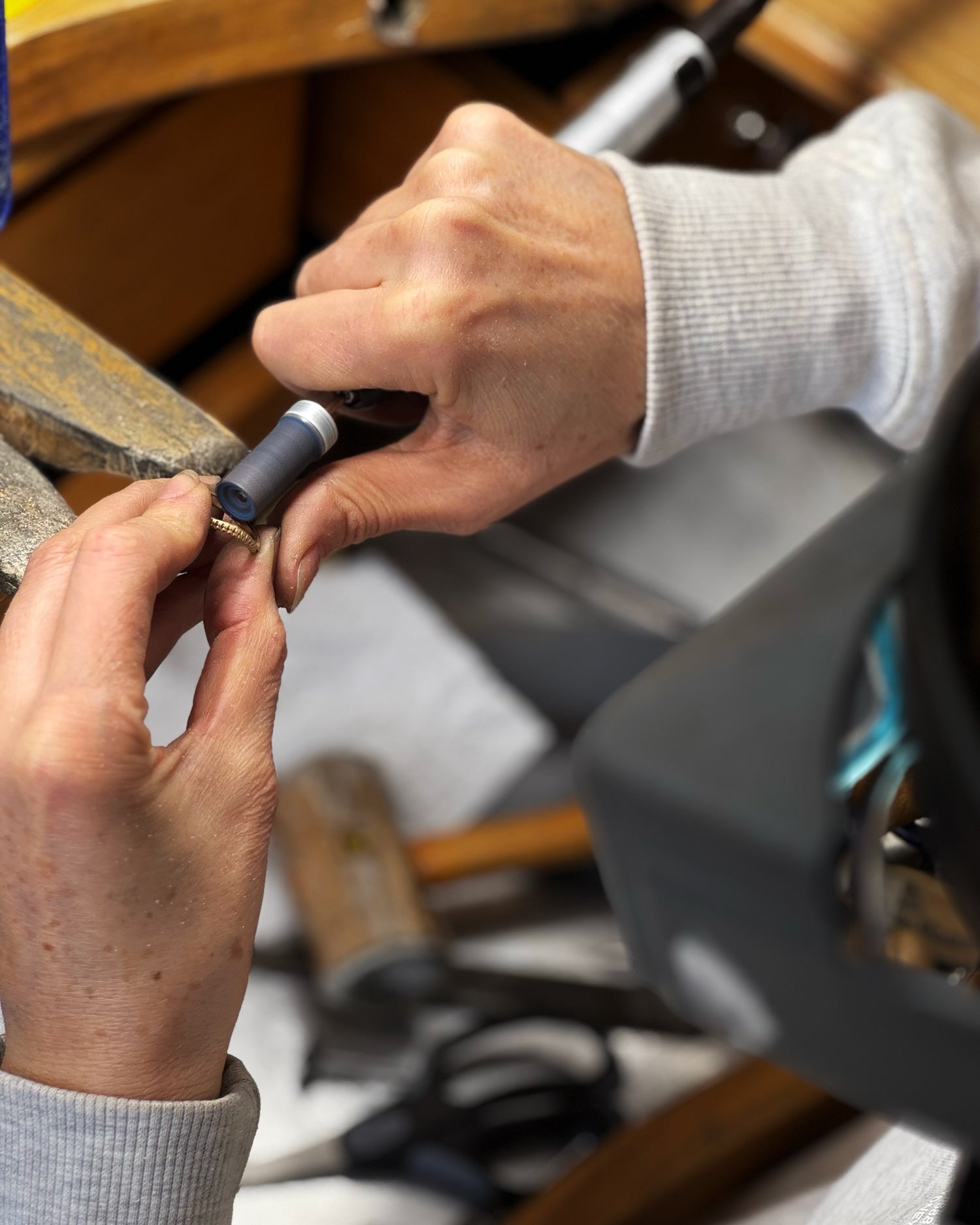 Close-up of hands working on a small object with tools in the background