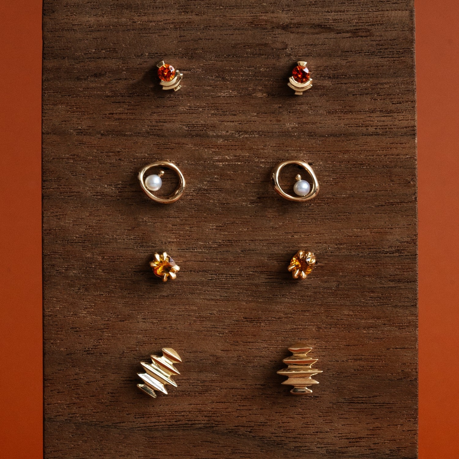 Four sets of stud earrings by Goldpoint Jewelry on a wooden display with orange backdrop