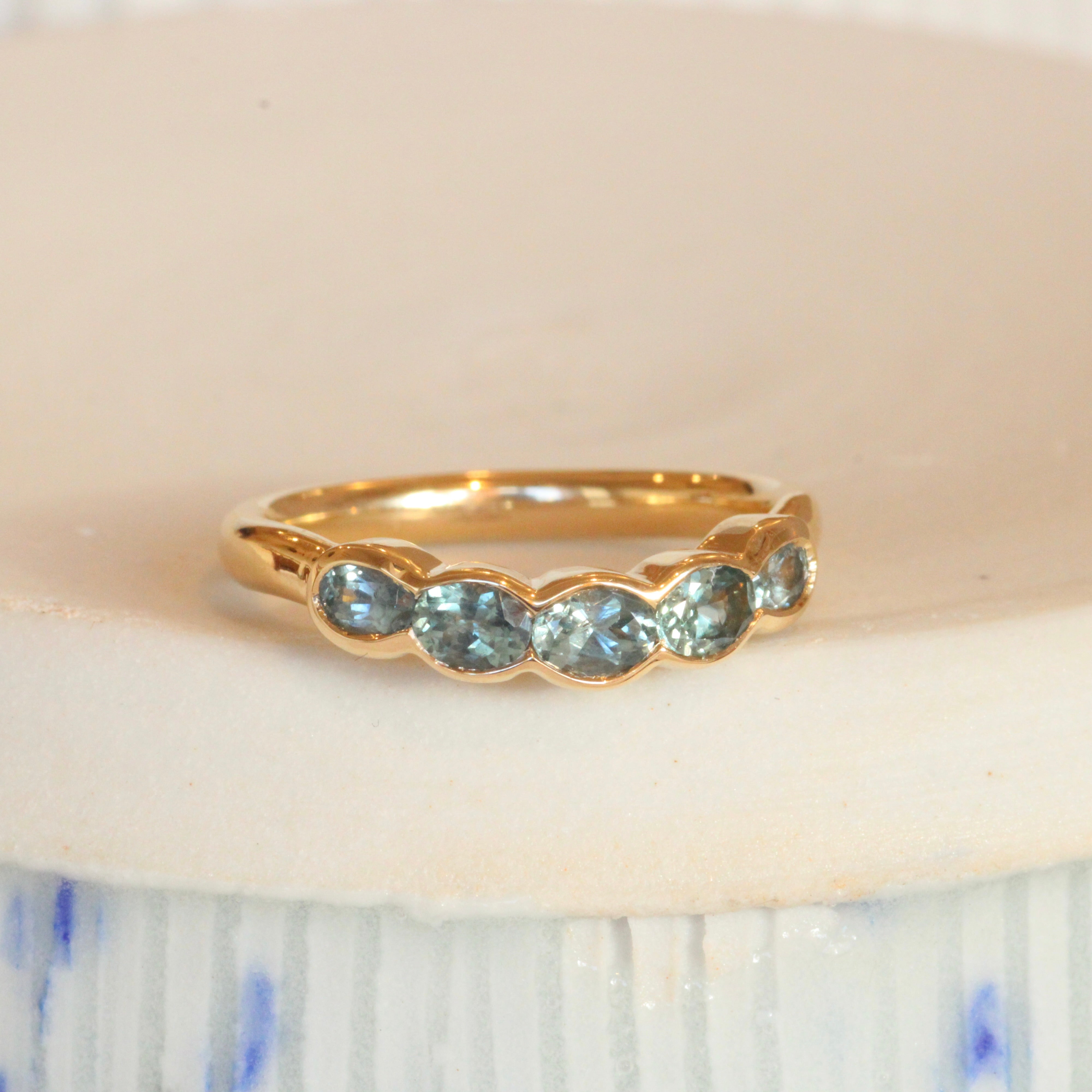 Lifestyle angled view of Cloud 5 Band Curve / Oval Sapphires in 14k yellow gold by Goldpoint Jewelry on a ceramic