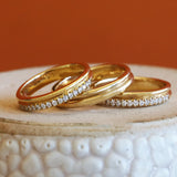 Lifestyle stacked front view of Duo Band / Pave Round Lab Diamonds, Duo Band, and Duo Band / Pave Round Natural Diamonds all in 14k yellow gold on a ceramic with orange background