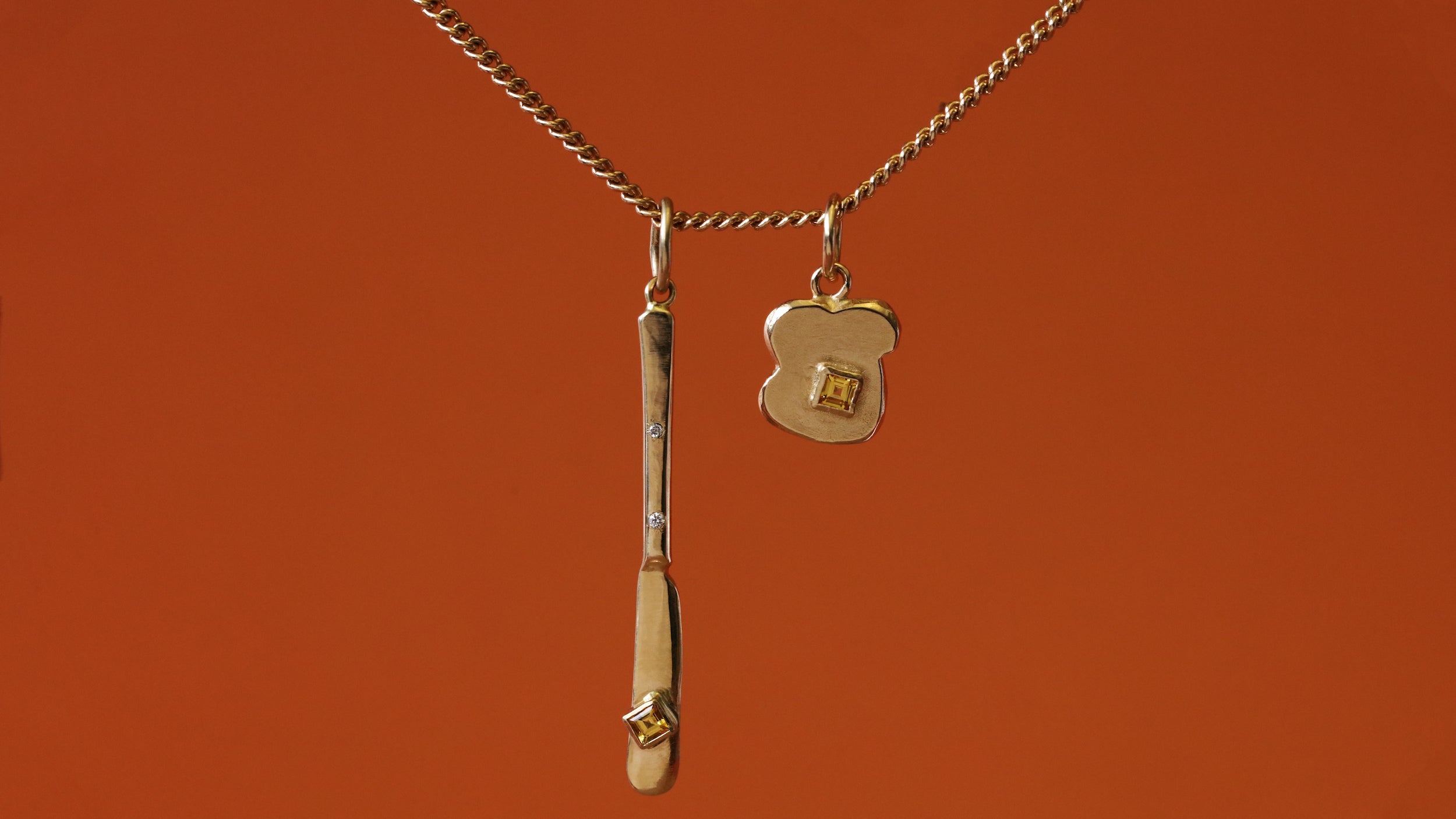 Pendant featuring Fancy Butter Knife Charm / Princess Cut Sapphire and Toast Charm / Princess Cut Sapphire in 14k yellow gold by Oxbow Designs on a orange background