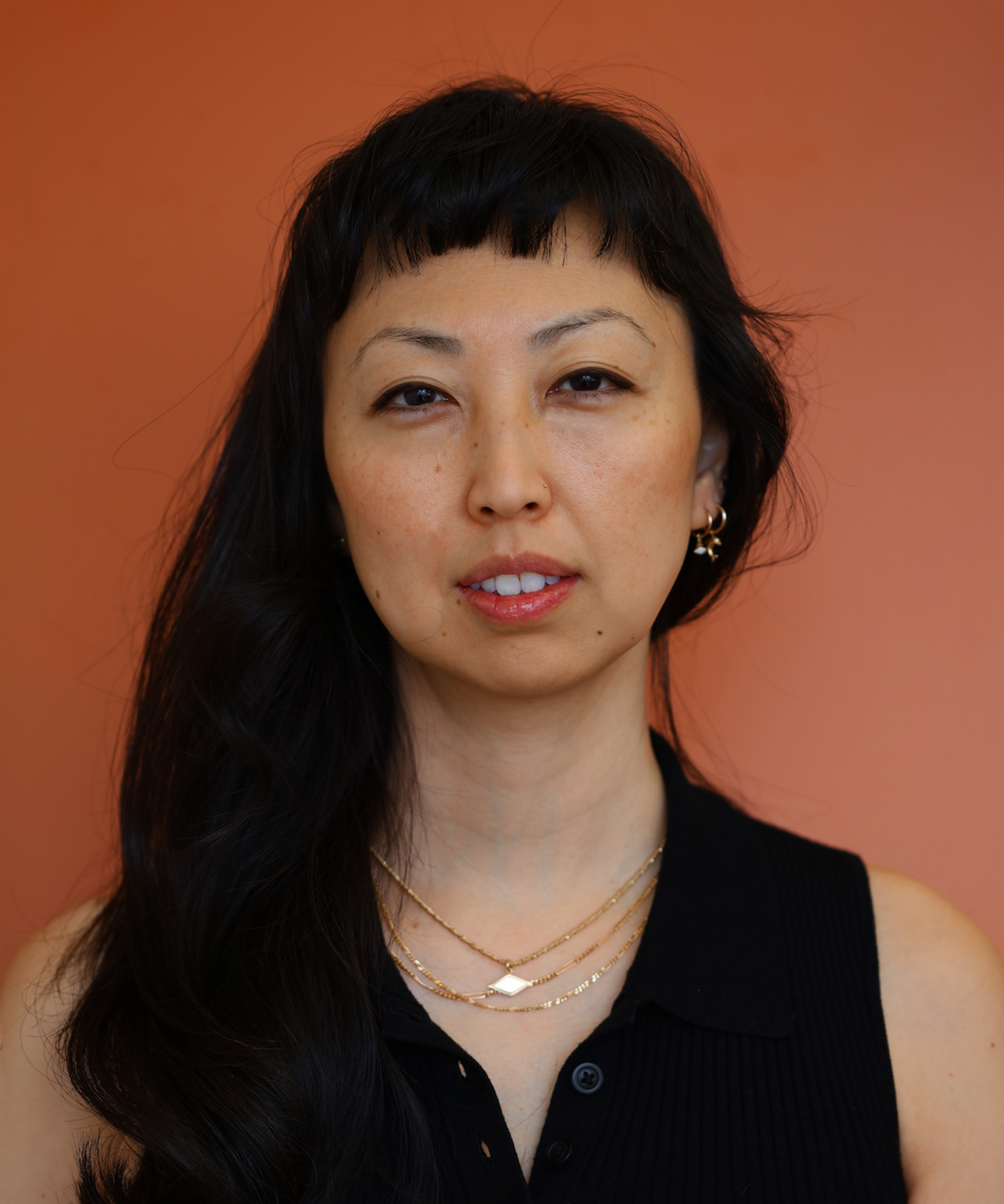 Portrait of Sunim Choi co-founder of Goldpoint Jewelry on a orange backdrop