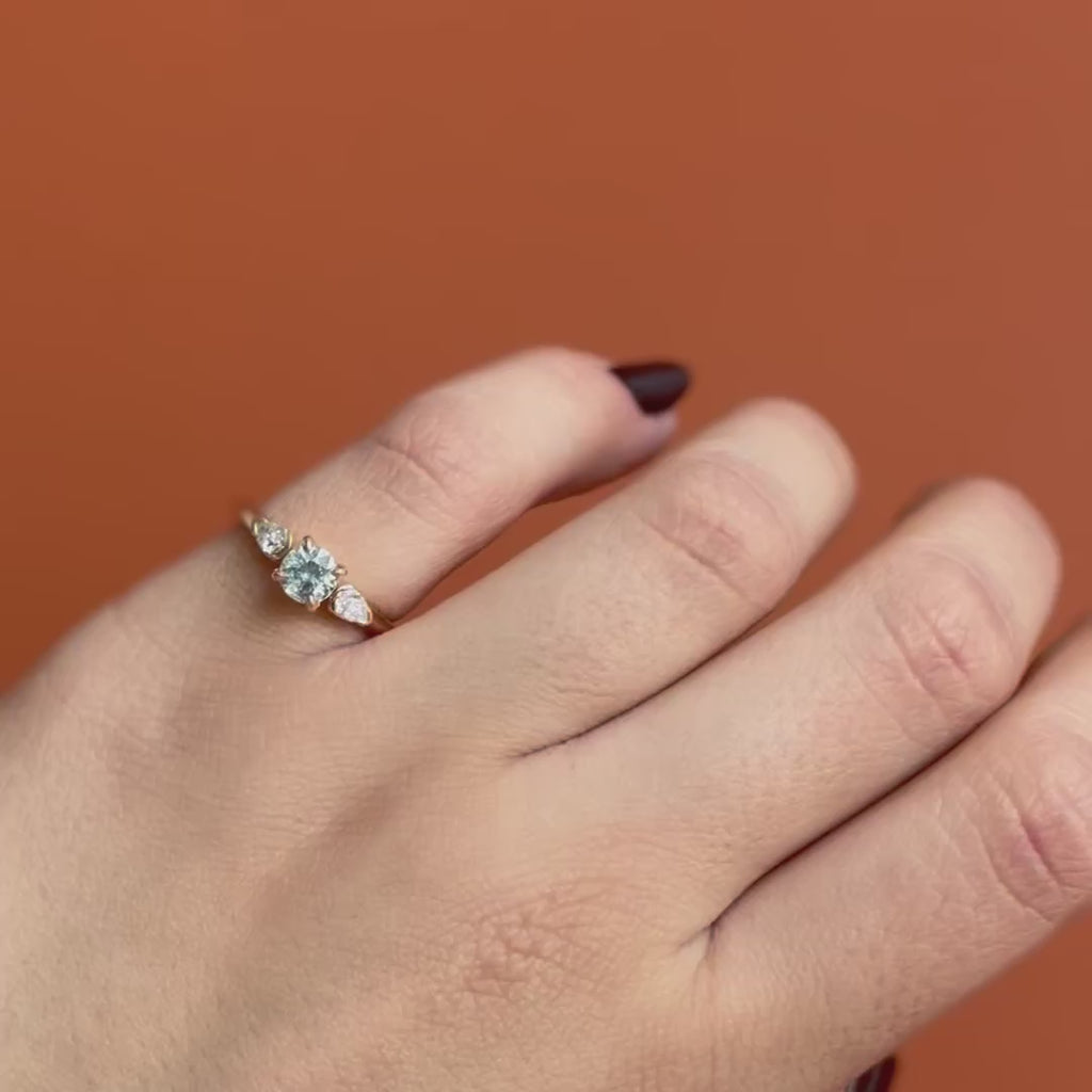 Model wears Wythe Ring Round Sapphire 0.69ct by Goldpoint Jewelry on pinky finger showing different angles over an orange backdrop