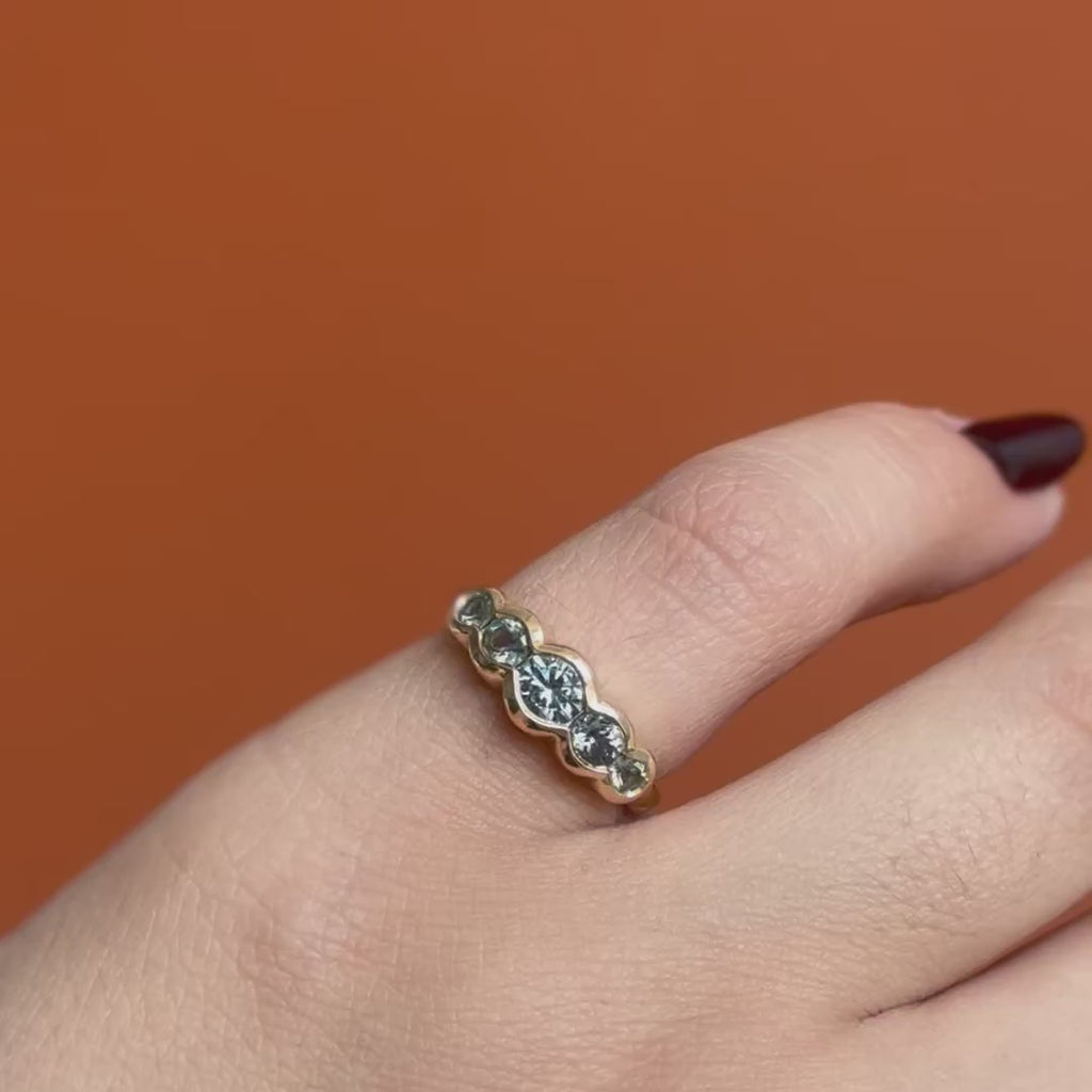 Model wears Clay 5 Ring Round Sapphires 0.4ct by Goldpoint Jewelry on pinky while showing different angles over an orange backdrop