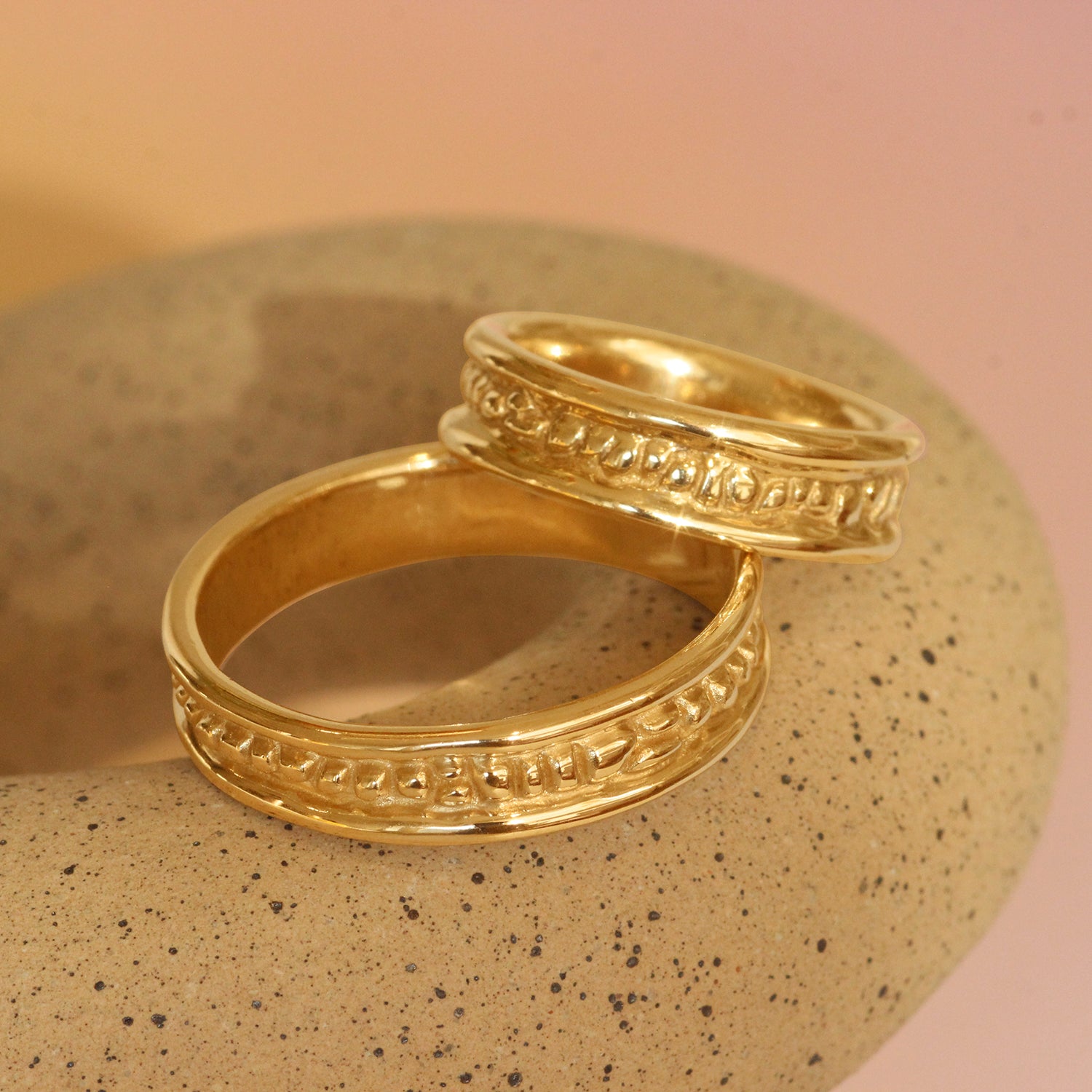 Lifestyle stacked view of two pieces of Ruins Band Polished Sides in 14k yellow gold by Goldpoint Jewelry on a ceramic with a pink neutral backdrop