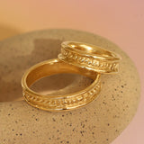 Lifestyle stacked view of two pieces of Ruins Band Polished Sides in 14k yellow gold by Goldpoint Jewelry on a ceramic with a pink neutral backdrop