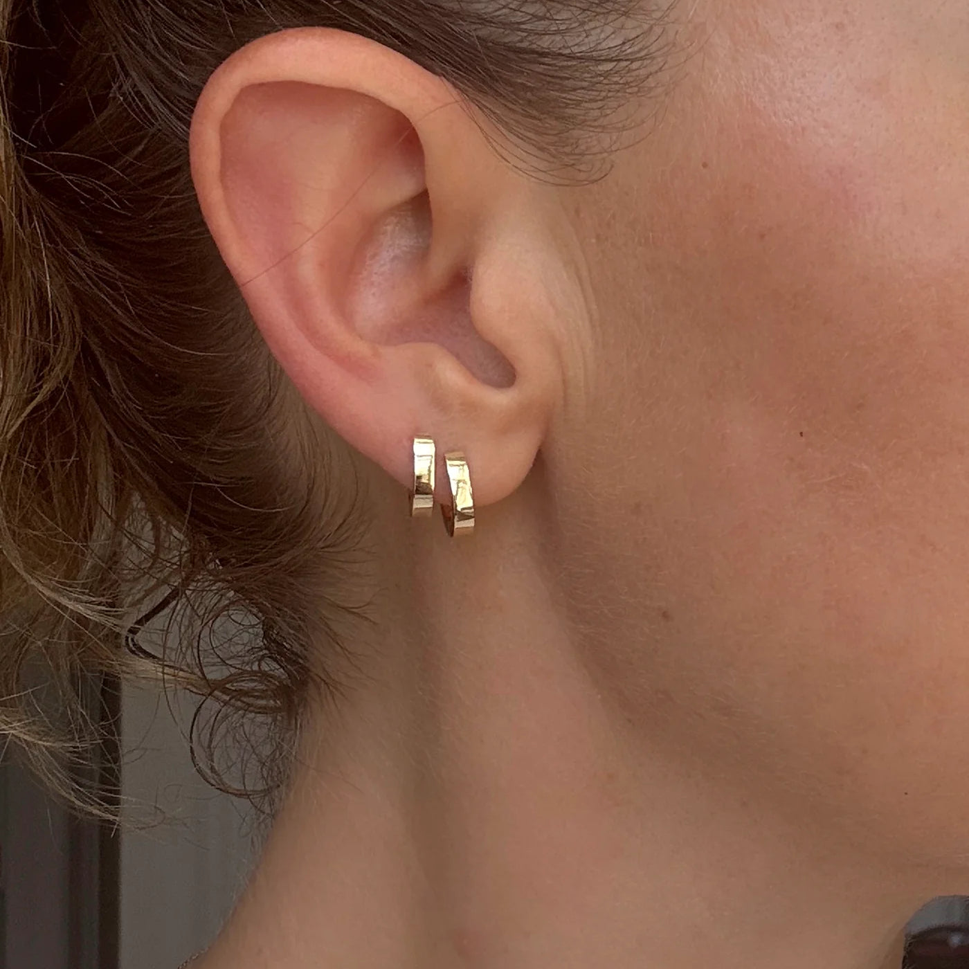 Model wears a set of Solid Huggie Hoops by Mon Pilar in ear