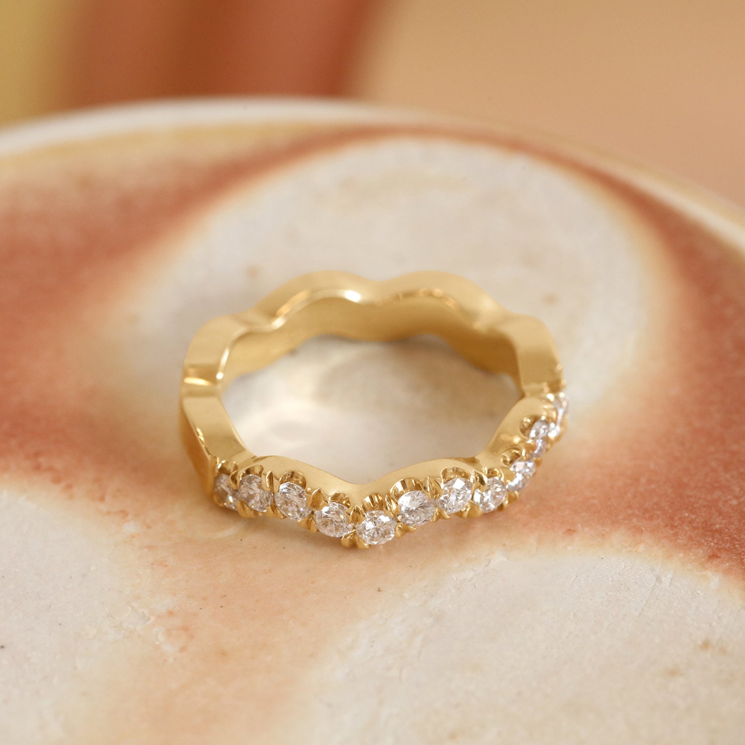 Lifestyle angled view of Waves Band Pave Round Lab Diamonds in 14k yellow gold by Goldpoint Jewelry on a ceramic