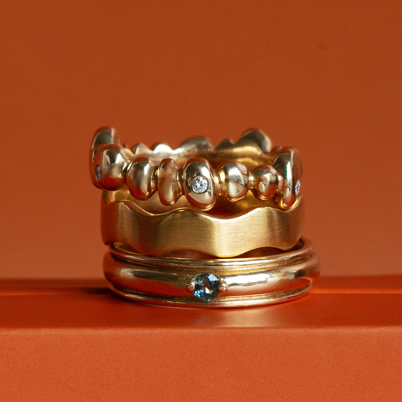 A stack of three various styled wedding bands by Goldpoint Jewelry on an orange backdrop