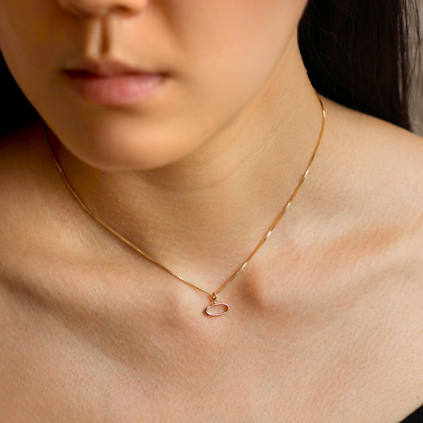 Woman wearing an amorphous circle charm on a gold chain.