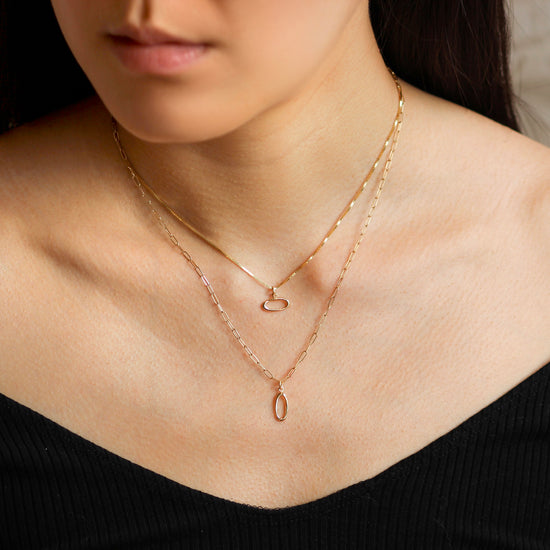 Model wears Amorphous Charm / Oval Longways by Goldpoint on a chain as a necklace with another necklace configuration with Amorphous Charm / Oval Sideways on a chain